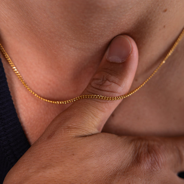 2mm gold curb chain necklace worn around the neck with hand holding the chain, close-up view