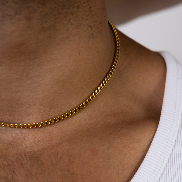 A close-up of models neck and upper chest wearing a 4mm gold cuban chain necklace and a white ribbed tank top.