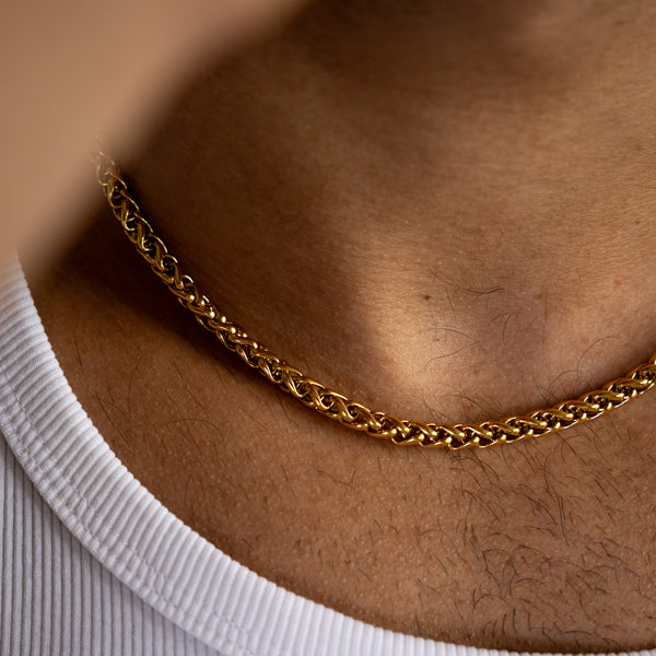5mm gold wheat chain necklace worn around the neck whilst weaing white vest, close-up view