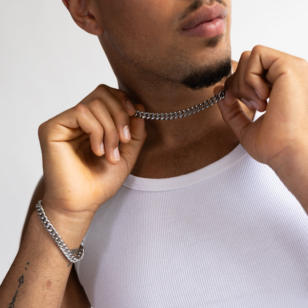 8mm silver Cuban bracelet and matching chain with hand holding chain, worn with a white tank top, close-up view