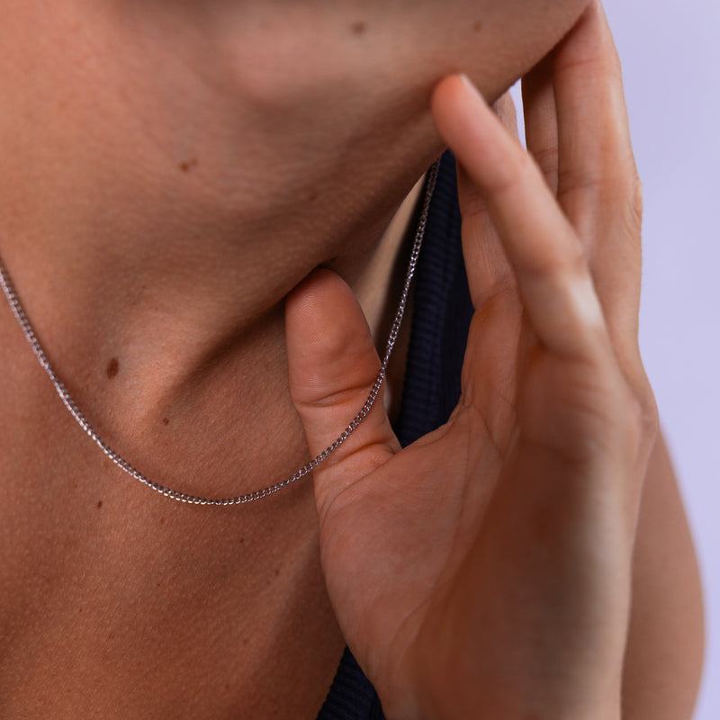 2mm silver curb chain necklace worn around the neck with hand holding the chain, close-up view