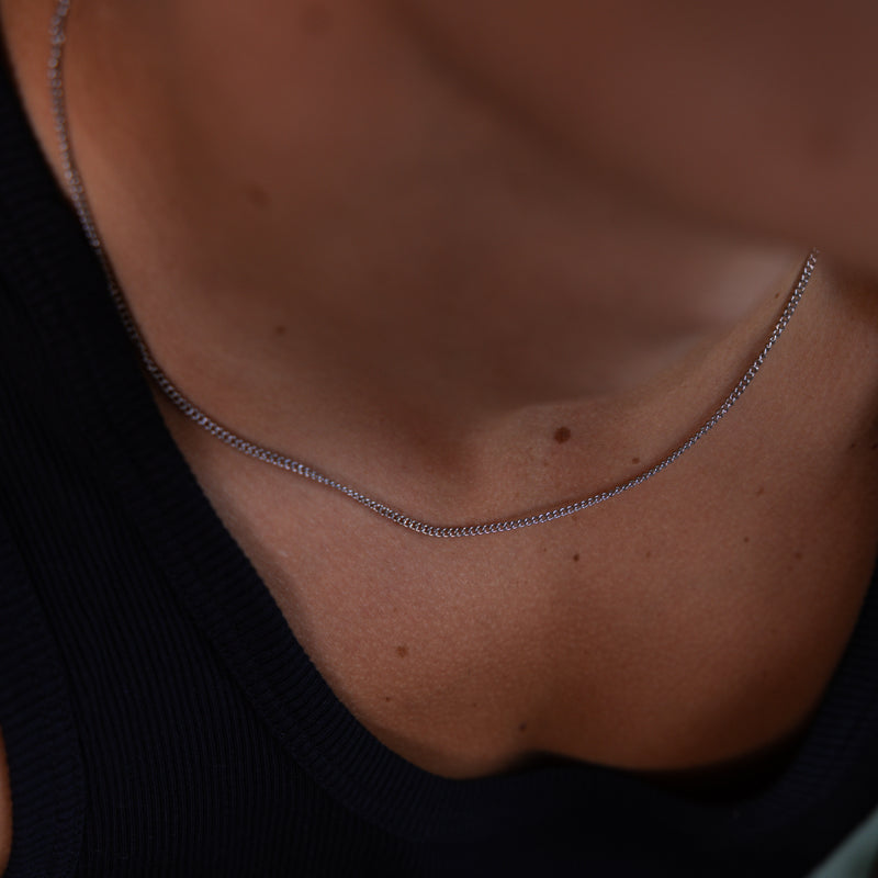 2mm silver curb chain necklace worn around the neck whilst weaing black vest, close-up view