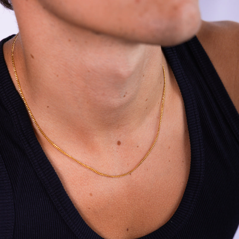 2mm gold curb chain necklace worn around the neck wearing black vest