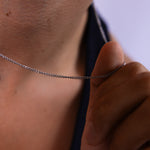 2mm silver curb chain necklace worn around the neck with hand holding the chain, close-up view