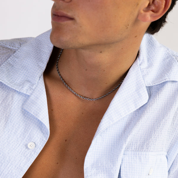 Silver rope chain necklace worn around the neck with an open white shirt, front angled view