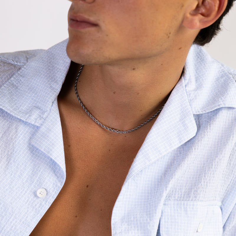 Silver rope chain necklace worn around the neck with an open white shirt, front angled view