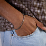 Silver curb chain bracelet worn on the wrist with hand in jeans pocket, close-up view