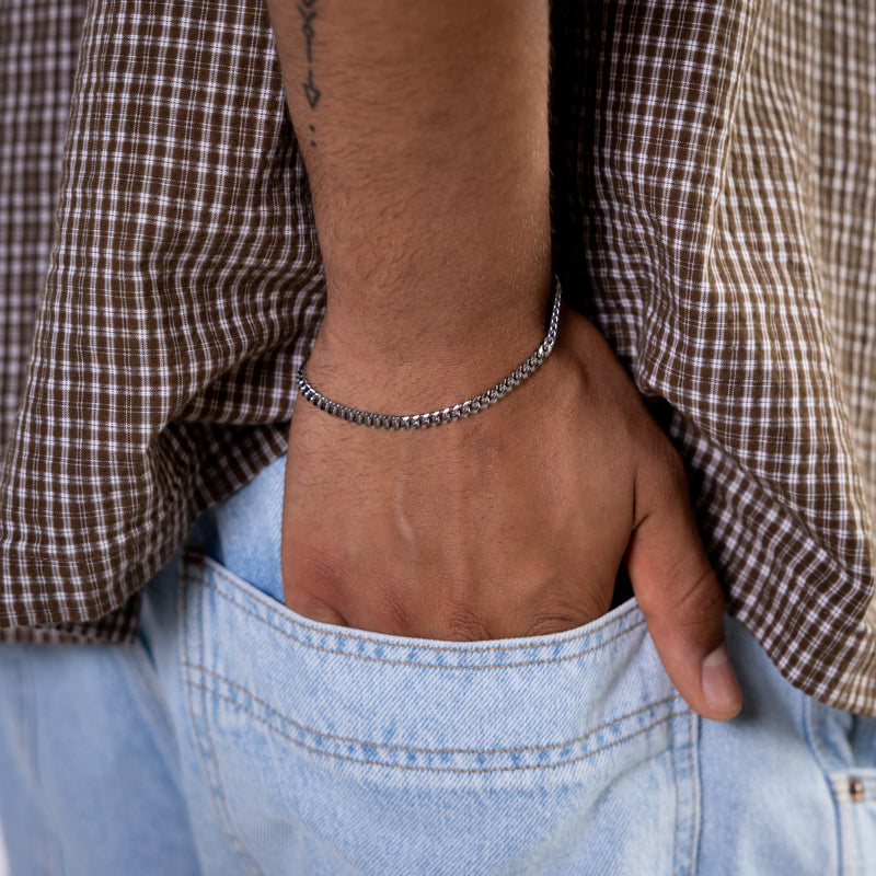 Silver curb chain bracelet worn on the wrist with hand in jeans pocket, close-up view