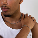 Silver curb chain necklace and matching silver curb chain bracelet worn with a white tank top, close-up view