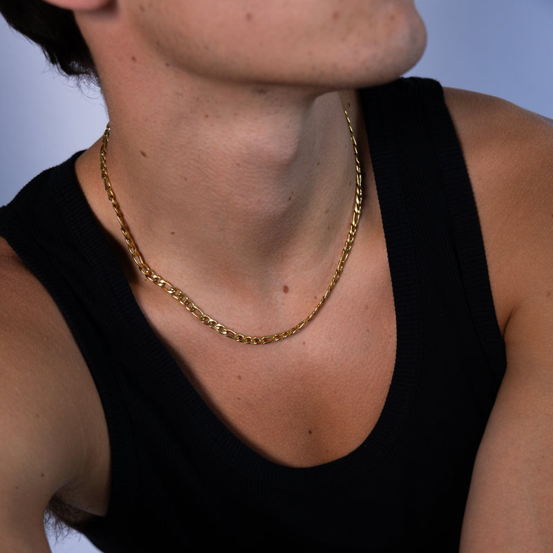5mm gold Figaro chain necklace worn around the neck with a black tank top, close up front view