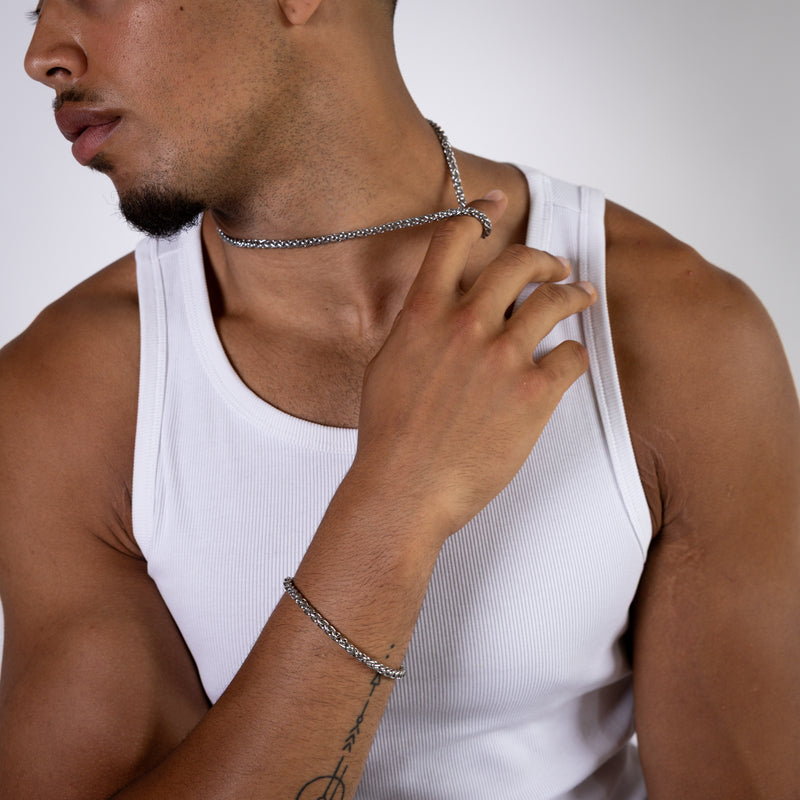 5mm silver wheat chain necklace worn around the neck with hand holding the chain, far away view