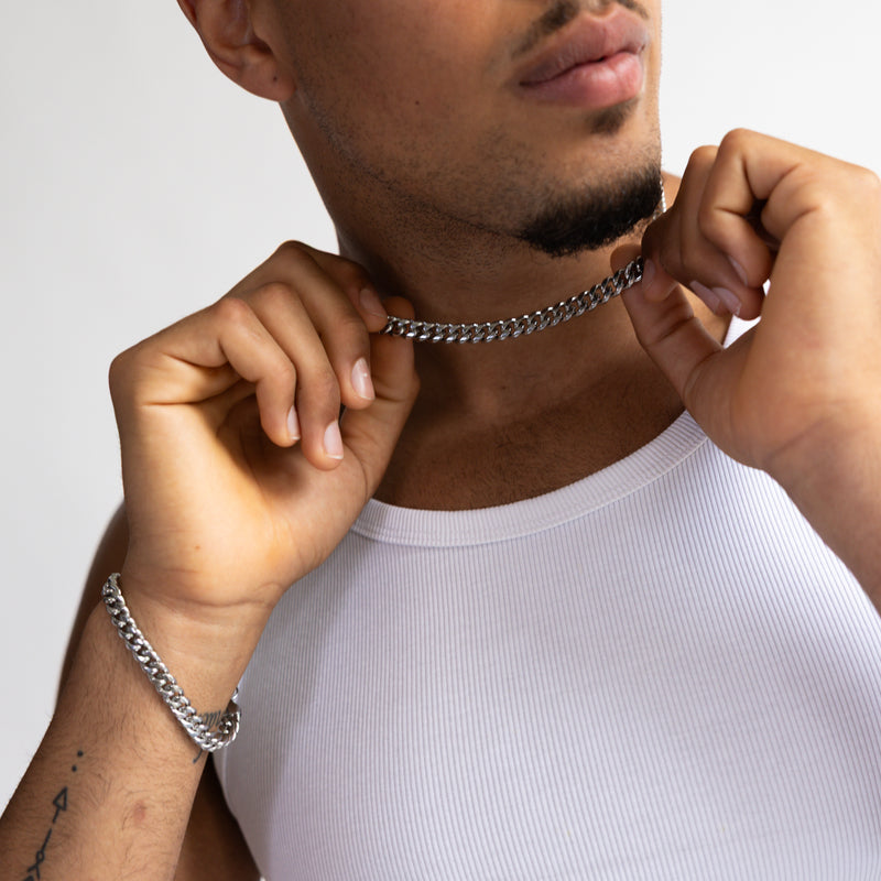 8mm silver Cuban bracelet and matching chain with hand holding chain, worn with a white tank top, close-up view