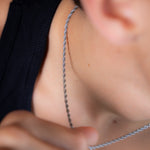 Silver rope chain necklace worn around the neck with black vest, close up view